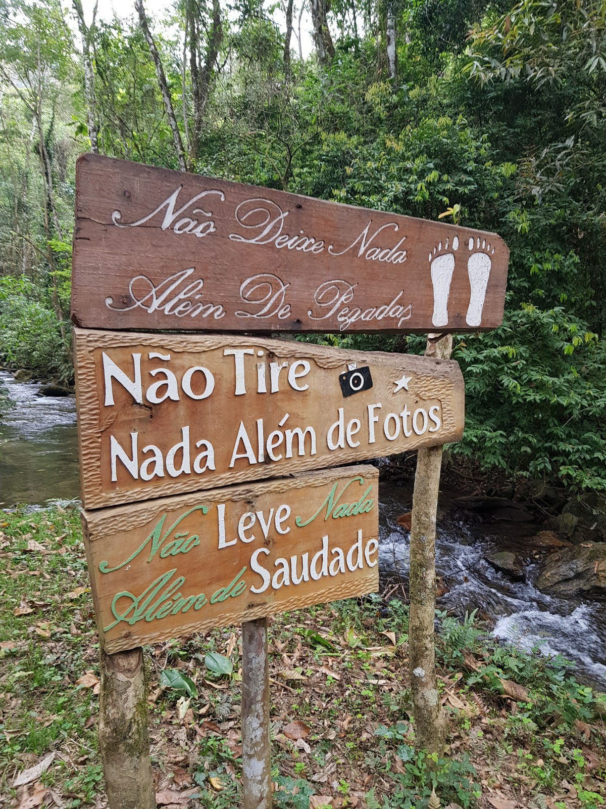 Fotografia de uma placa na mata escrita: Não deixe nada além de pegadas. Não tire nada além de fotos. Não leve nada além de saudades